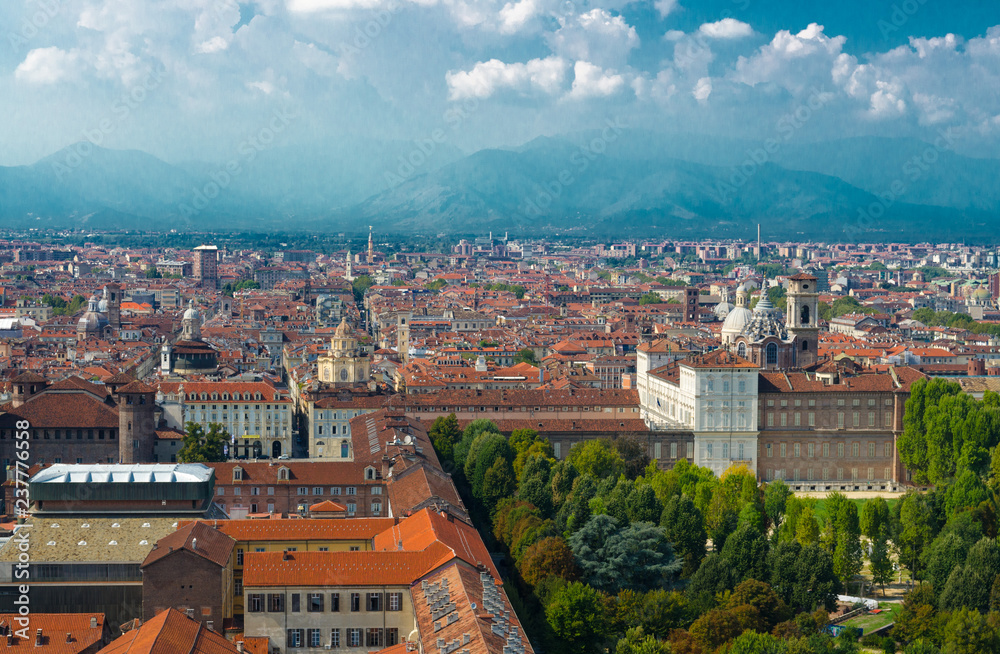 Aerial top panoramic view of Turin city historical centre with Royal Palace, San Lorenzo church, orange tiled roofs of buildings, Giardini Reali gardens park with Alps mountain range, Piedmont, Italy