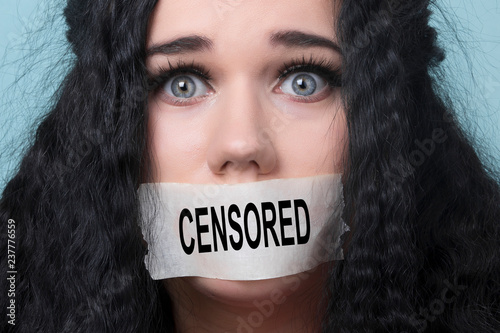 portrait of young woman with mouth and lips sealed in adhesive tape restrained and abused censored and banned to speak, concept of hostage