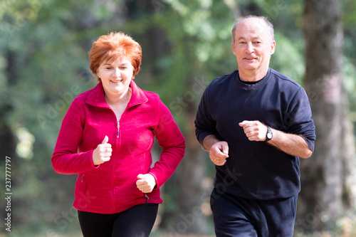 Senior couple wearing sportswear and running in forest
