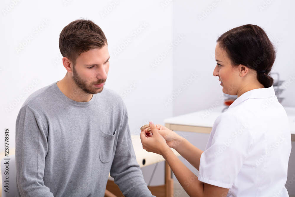Man Looking At Doctor Holding Hearing Aid Man Looking At Doctor Holding Hearing Aid