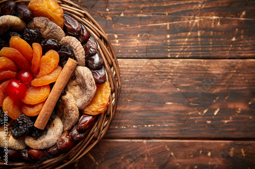 Mix of dried fruits in a small wicker basket on wooden table. Assortment contais apricots, plums, figs, dates, cherries, peaches. Above view with copy space. photo