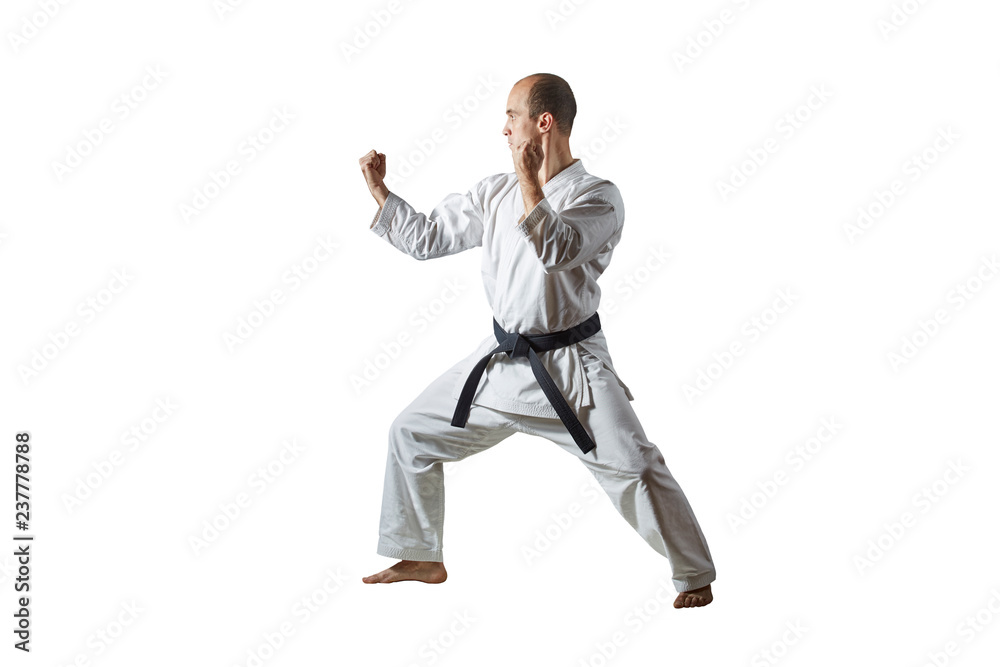 On a white isolated background an athlete with a black belt trains formal karate exercises On a white isolated background an athlete with a black belt trains formal karate exercises