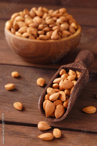 Dry apricot kernels in a wooden bowl and scoop on a wooden background.