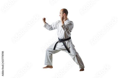 On a white isolated background an athlete with a black belt trains formal karate exercises