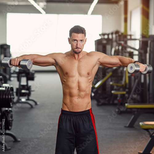 Strong healthy man training his shoulders in the gym. Isolated exercise for training deltoid muscle. Work out at the modern gym.