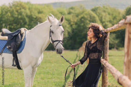 Young woman in black dress with her white horse outdoor