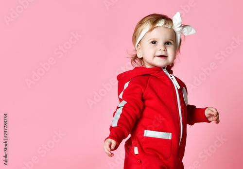 Infant child baby boy kid toddler in redbody cloth make first steps standing happy looking up on light pink 
