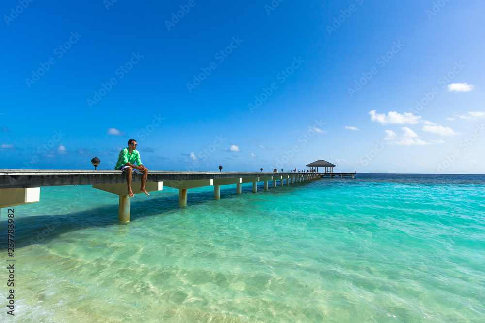 Junger Mann mit grünem Hemd sitzt auf einem Steg auf den Malediven