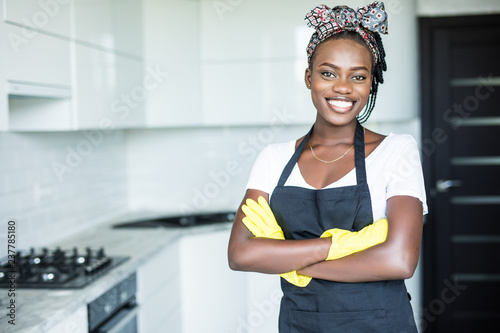 Smiling african american housewife in apron with arms crossed cleaning at home photo