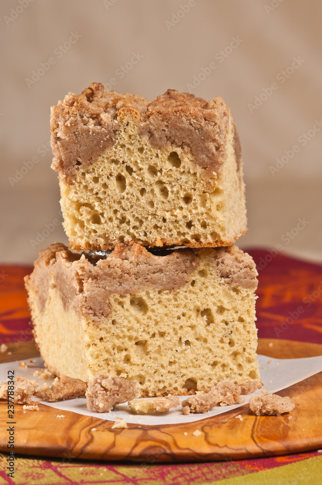Top, front, close up, of two stacked squares of freshly baked, homemade, crumb coffee cake on a square, white plate with a print, cloth napkin