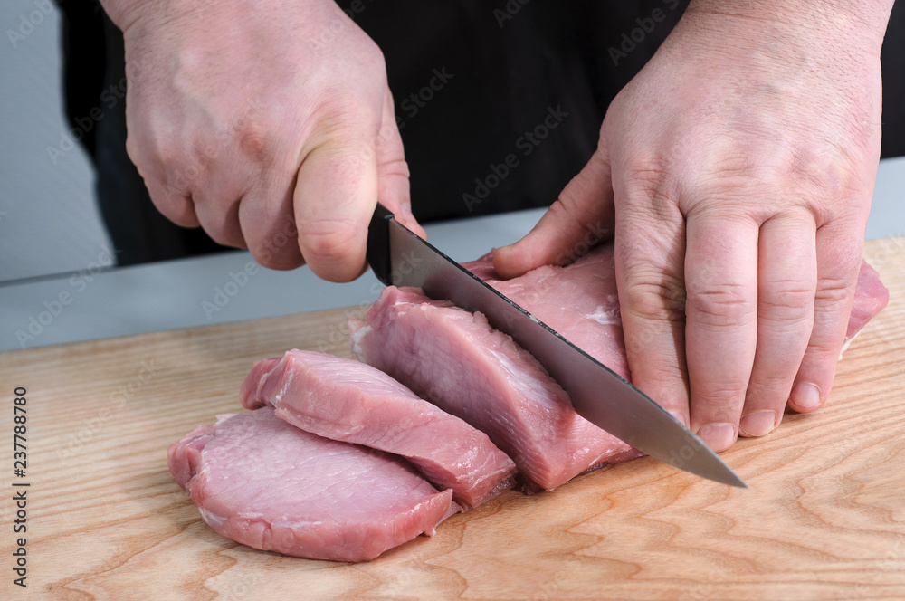 Closeup view man in the kitchen is cutting pork on cutting board Hands cutting meat