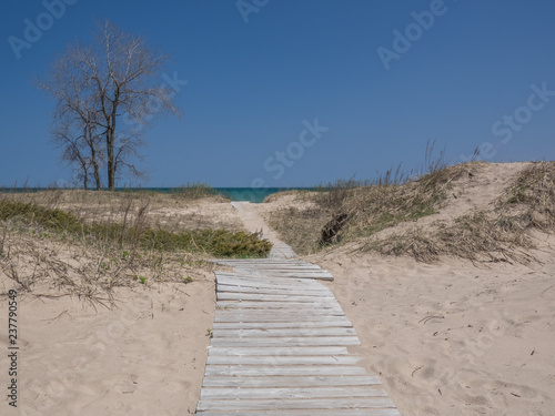 Sandy  broken boardwalk leads over a sand dune to aqua water at a deserted beach along Lake Michigan.