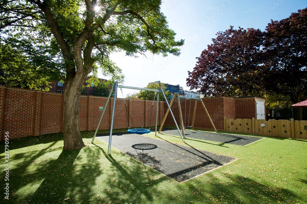 Modern safe playground with a large swing rubber mat and astroturf in an enclosed yard on a sunny day.