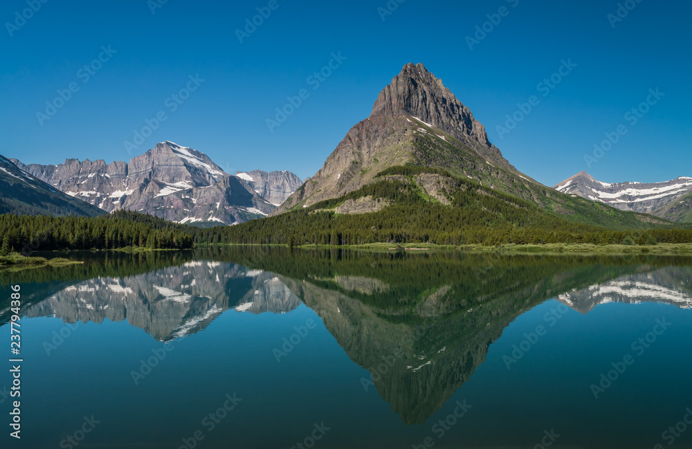 Naklejka premium Odbicie jałowej góry górującej nad jeziorem Swiftcurrent w piękny letni dzień w Glacier National Park