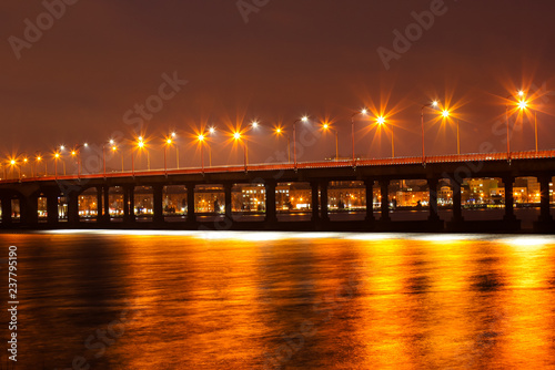 Beautiful winter view of the bridge, lanterns light reflected on the ice of the Dnieper River. Dnipro city, Ukraine. Dnepropetrovsk, Dnipropetrovsk