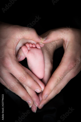 Baby's foot in hands dark black background love heart shape 