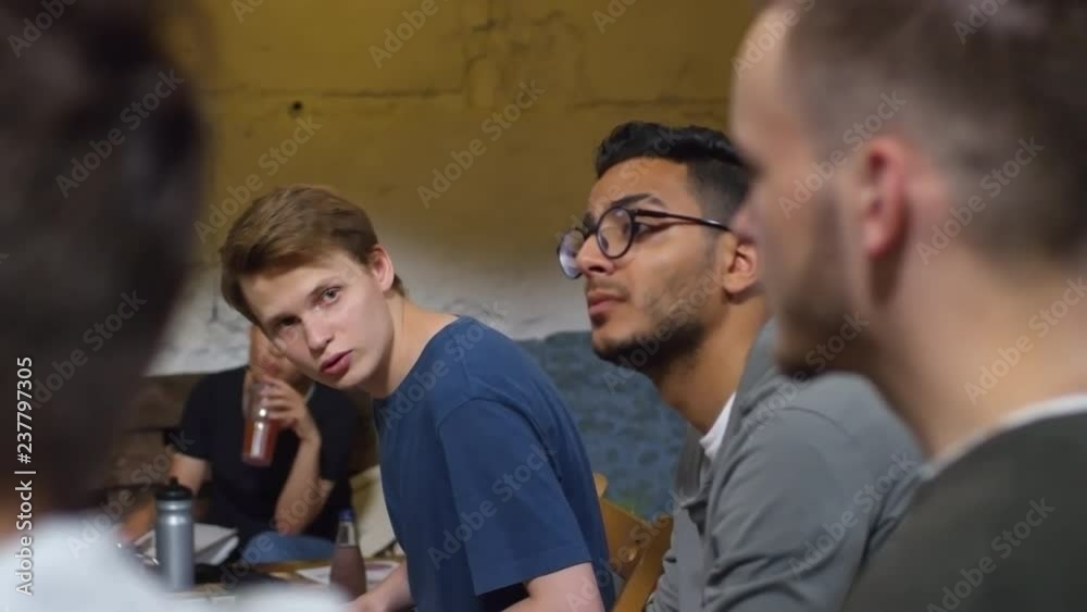Medium shot of group of multiethnic young people sitting in chairs and listening to presentation or lecture, one of them asking question to the other Medium shot of group of multiethnic young people sitting in chairs and listening to presentation or lecture, one of them asking question to the other