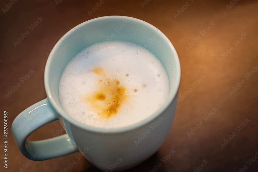 Cappuccino in a pastel blue cup on a brown table, visible white coffee foam Cappuccino in a pastel blue cup on a brown table, visible white coffee foam