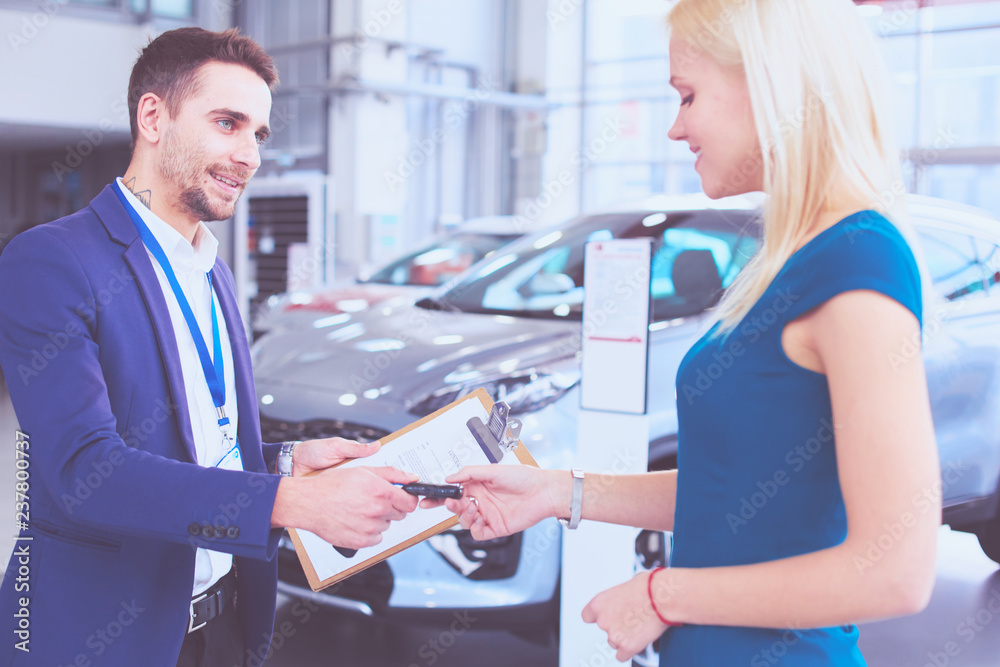 Obraz premium Car salesman sells a car to happy customer in car dealership and hands over the keys