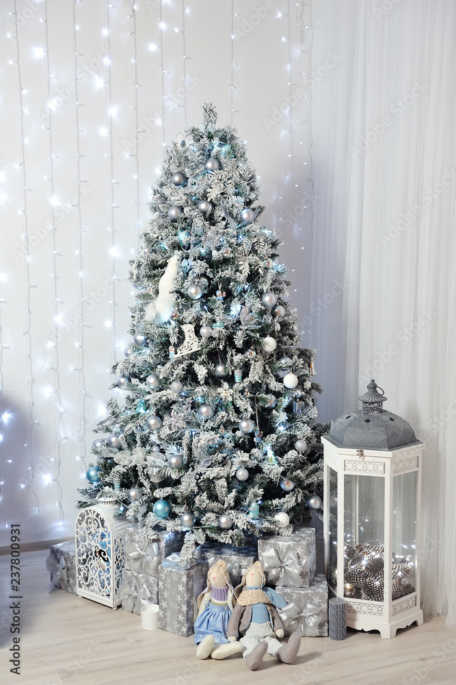 New Year's Decor in a photo studio in gray and white. A snow-white Christmas tree, gifts and lanterns, against the background of a white wall with a garland