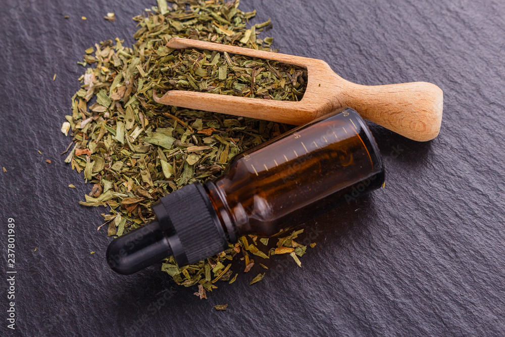 dried tarragon and essential oil on a dark stone background