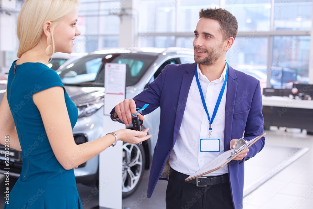 Fototapeta premium Car salesman sells a car to happy customer in car dealership and hands over the keys