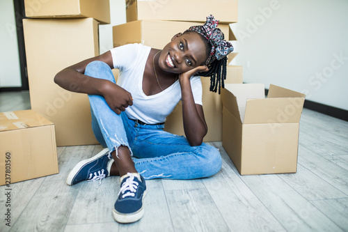Moving in. Charming young african girl standing on her knees on the floor and smiling at the camera while taking plates out of the box