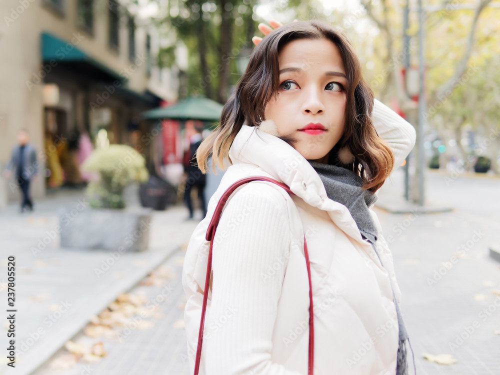 Fototapeta premium Beautiful brunette woman looking back with hands on head in sunny autumn day. Outdoor fashion portrait of glamour young Chinese business stylish lady. Emotions, people, beauty and lifestyle concept.