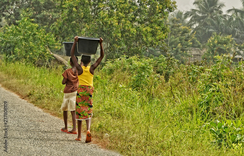 African teenagers carry a luggage on their heads. Young African girls walk along the road. Countryside. Lifestyle in developing countries of Africa. Ghana, Accra - January 31, 2017