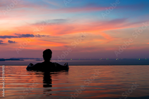 Black silhouette of asian woman on summer vacation holiday relaxing in infinity swimming pool with blue sea sunset view. Healthy happiness lifestyle