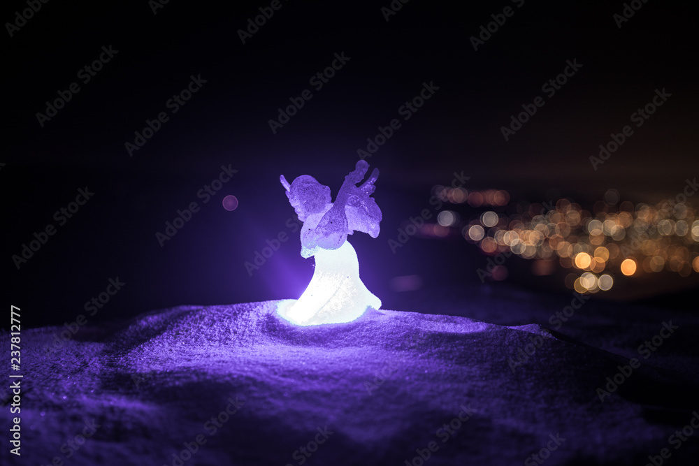 christmas angel on blur bokeh city lights at night on background. Little white guardian angel in snow. christmas angel on blur bokeh city lights at night on background. Little white guardian angel in snow.