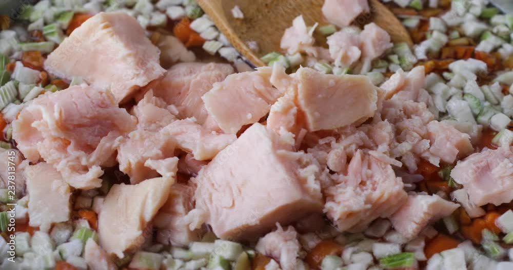 Close video of adding canned chicken to home made chicken noodle soup in a pan with a wood spoon in the background. Close video of adding canned chicken to home made chicken noodle soup in a pan with a wood spoon in the background.