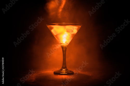 Martini in fire concept. Glass of famous cocktail Martini burning in fire at dark toned foggy background.