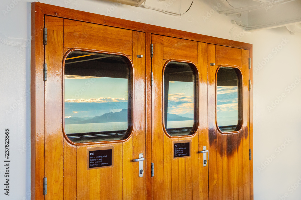 Cruise ship heavy varnished wood exterior doors with windows reflecting the sea.