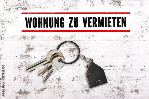 Nachricht "Wohnung zu vermieten" und Schlüssel mit Schlüsselanhänger in Hausform auf Steinuntergrund