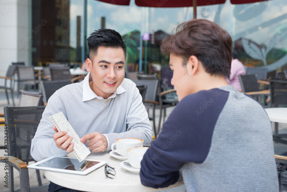 Two young handsome businessmen in casual clothes smiling, talking in coffee shop. Two young handsome businessmen in casual clothes smiling, talking in coffee shop.
