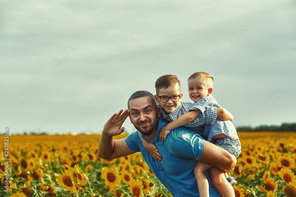 Cheerful loving father with his son on vacation in the field with sunflowers . The parent plays with his son . Father's day Cheerful loving father with his son on vacation in the field with sunflowers . The parent plays with his son . Father's day