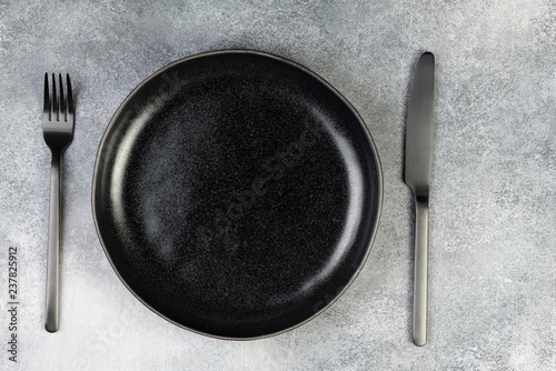 Obraz na płótnie Empty black plate, fork, knife, spoon on blue background, top view w salonie
