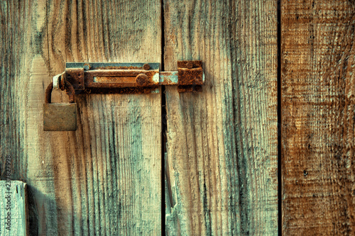 Old wooden door locked with rusty door latch and padlock.