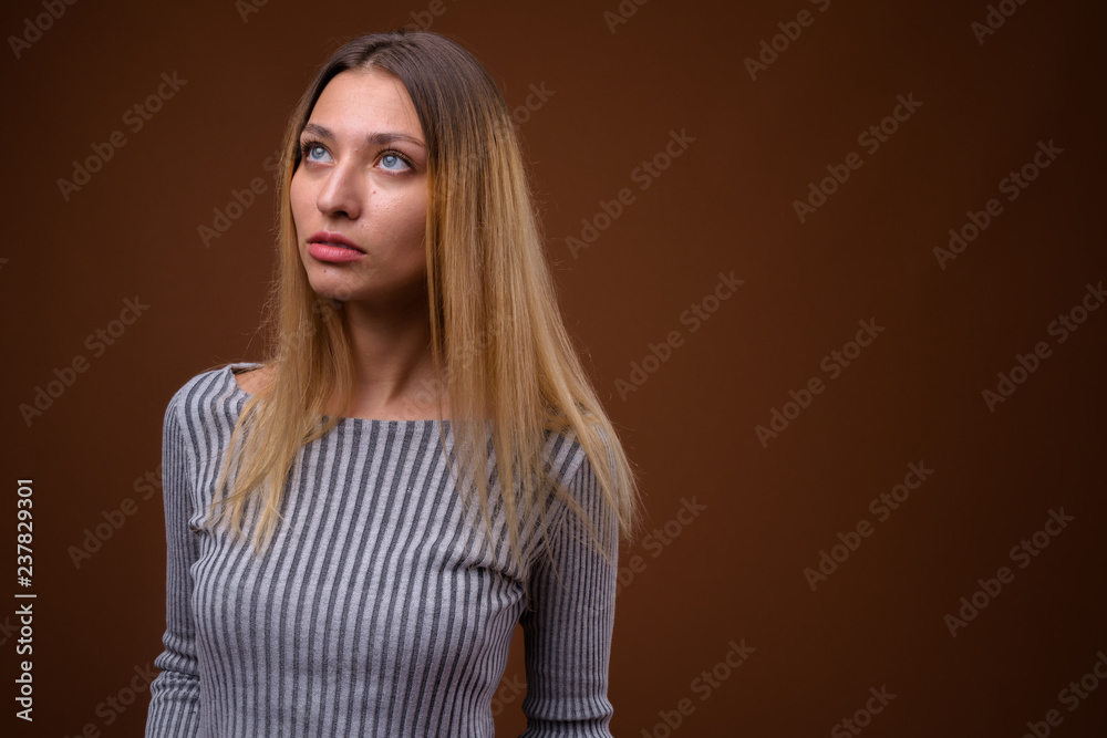 Studio shot of young beautiful woman thinking against brown background Studio shot of young beautiful woman thinking against brown background