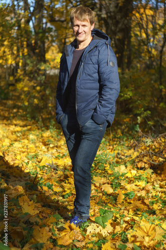 Confident young man standing in the autumn park with ancient castle in background and falling leaves in foreground. Horizontal outdoors shot. © Ruslan