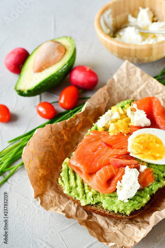 sandwich with avocado and salmon on a light background, green onions and gluten-free grain bread, radishes and tomatoes. concept diet food, copy space, sandwich take away, healthy fast food