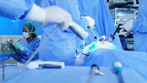 Multi ethnic surgical healthcare hospital training team in scrubs working in indoor theater facility preparing to perform Laparoscopic operation on patient  photo