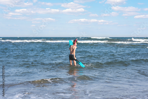 Happy teen boy in the swim flippers and snorkeling mask in the wave of the sea during summer vacation in the tropical resort town