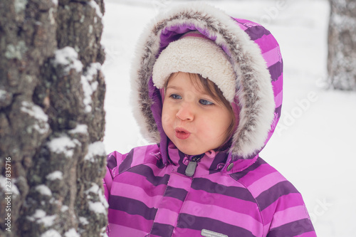 portrait of a little girl of Caucasian appearance in winter clothes, she is having fun and playing with snow