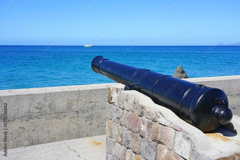 View of a colonial cannon pointed towards the Caribbean Sea in Charlestown, the capital of Nevis in the Federation of St Kitts and Nevis in the West Indies