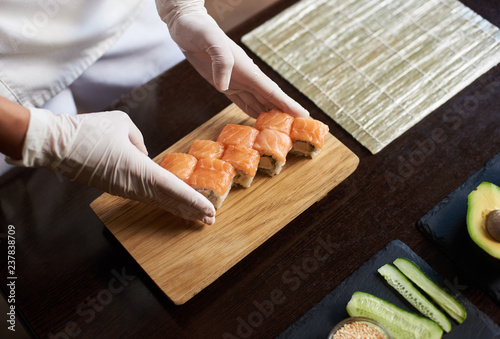 Close-up view of process of preparing rolling sushi. Chef is serving fresh delicious rolls on the wooden board