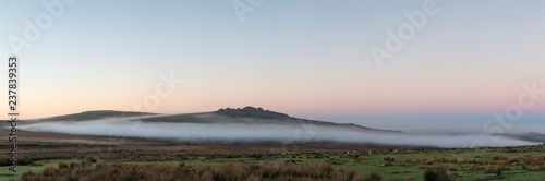 Beautiful foggy sunrise landscape over the tors in Dartmoor revealing peaks through the mist
