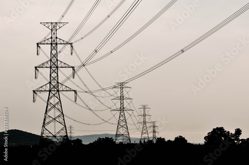 Group silhouette of transmission towers (power tower, electricity pylon, steel lattice tower) at cloudy sky in Thailand. Texture high voltage pillar, overhead power line, industrial background. 