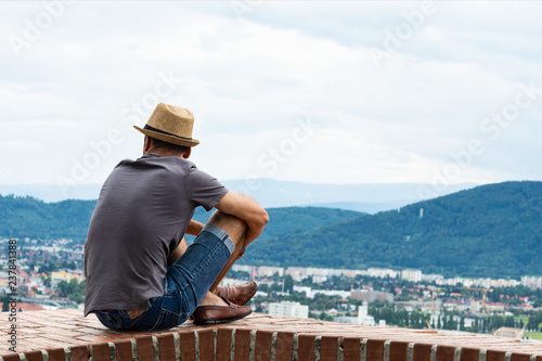 A young guy in comfortable moccasins sits on the edge of a tall building and looks at the mountains and the city of Graz photo